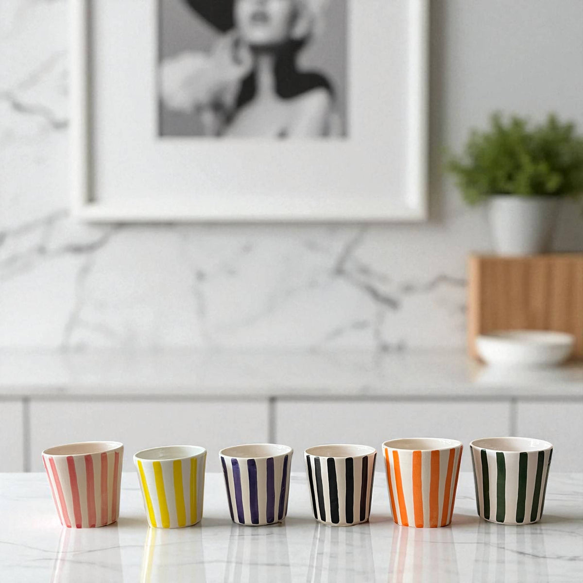 Set of colorful striped cups on a kitchen counter with a marble backsplash.