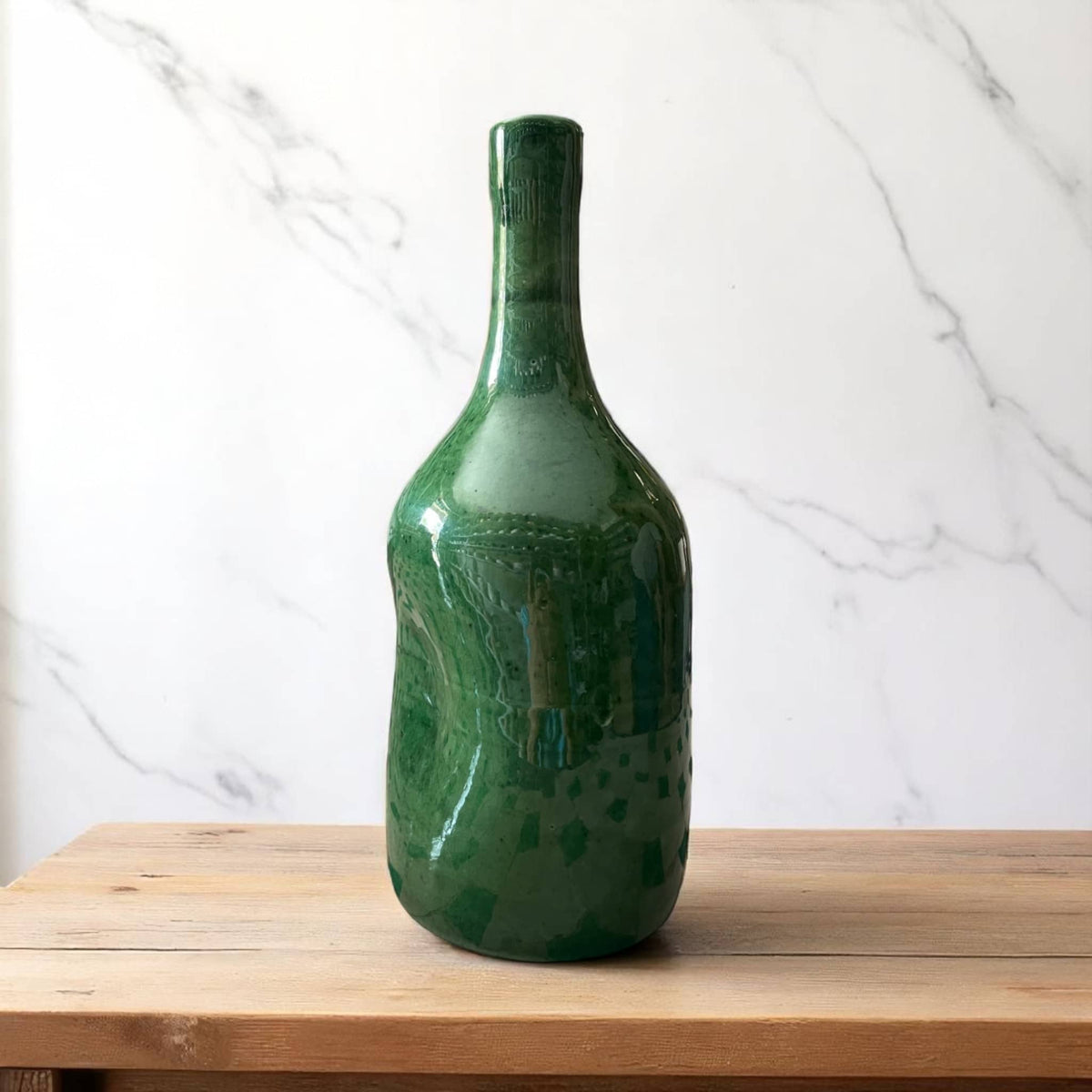 Green bottle vase on a wooden surface with a white marble background