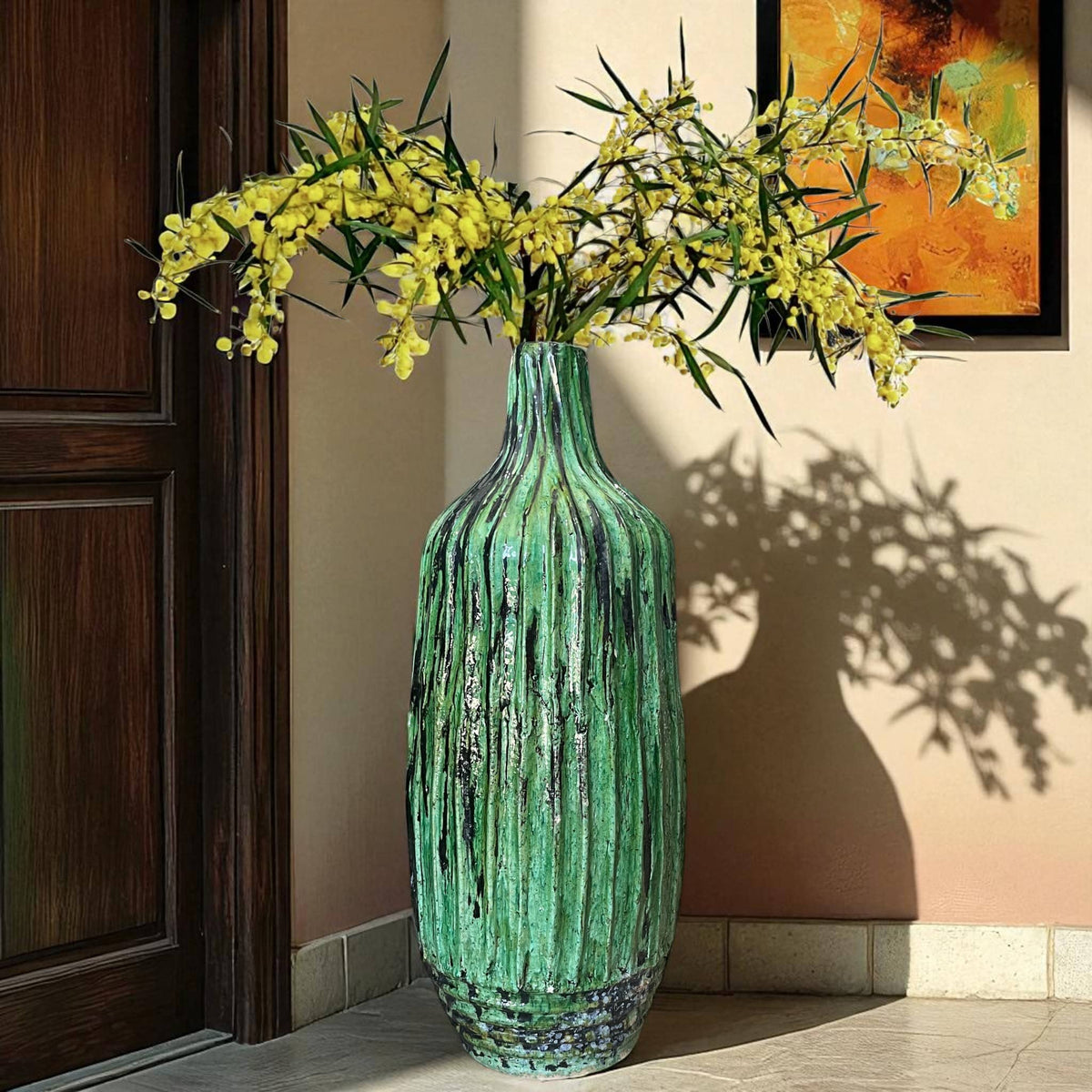 Green textured vase with yellow flowers against a beige wall.