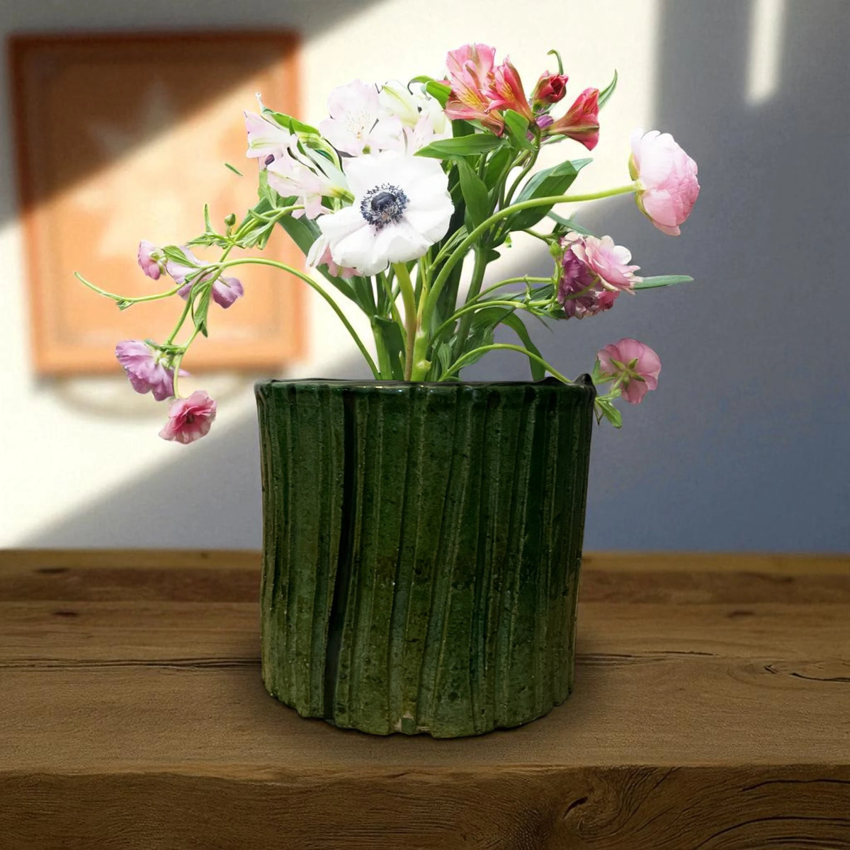 Green textured vase with flowers on a wooden surface