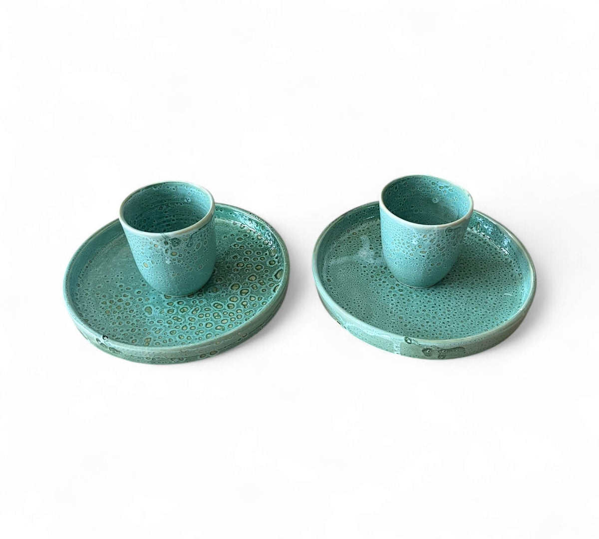 Two turquoise ceramic cups with matching saucers on a white background