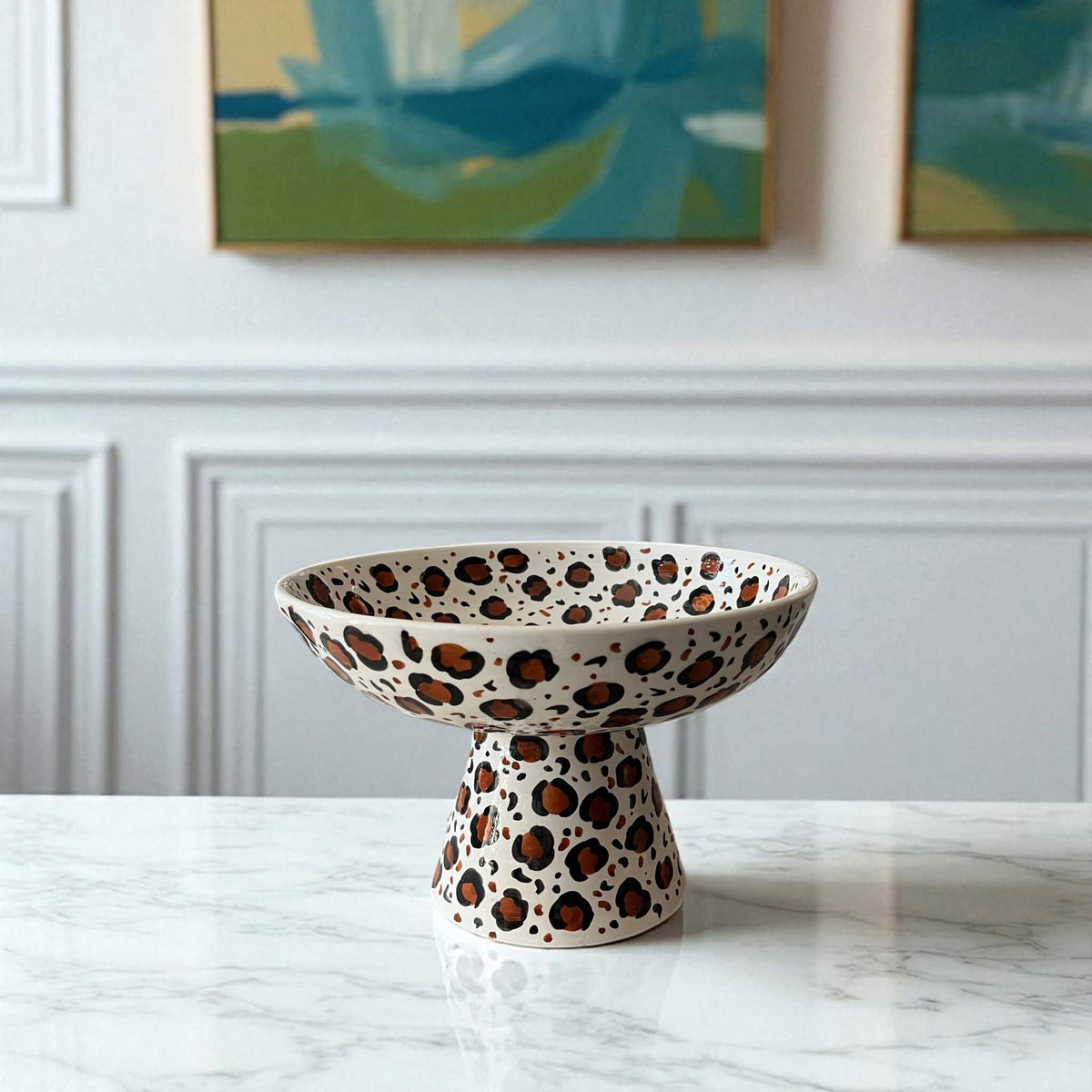 Ceramic bowl with leopard print design on a marble surface with a white wall and abstract art in the background.