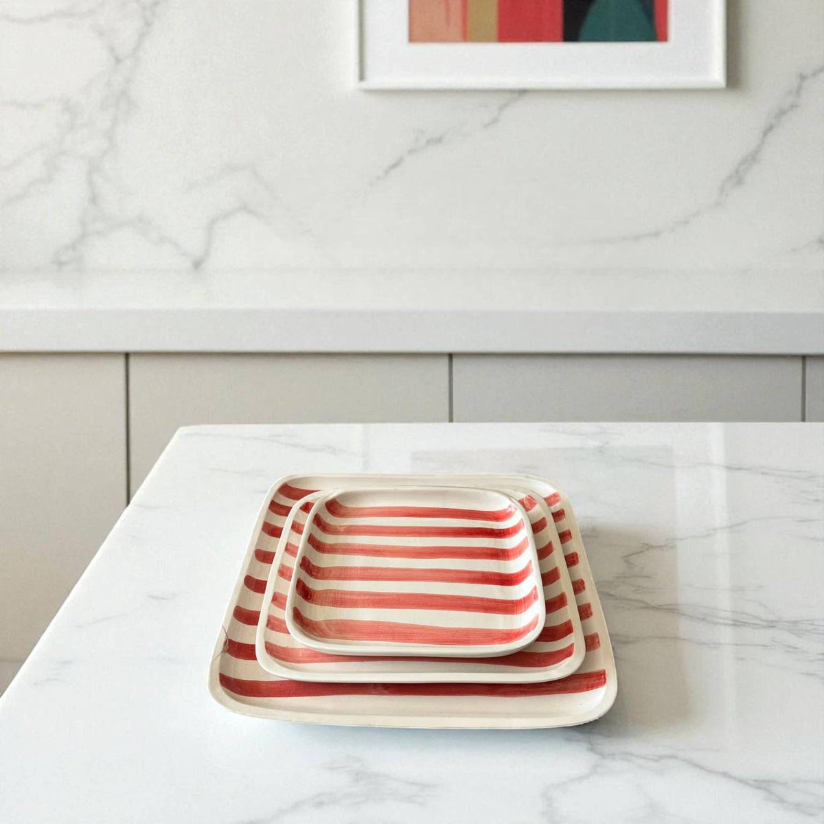Set of three rectangular ceramic trays with red and white stripes on a marble countertop.