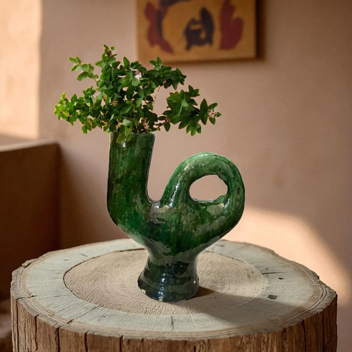 Green ceramic vase with plant on a wooden stump against a neutral wall.