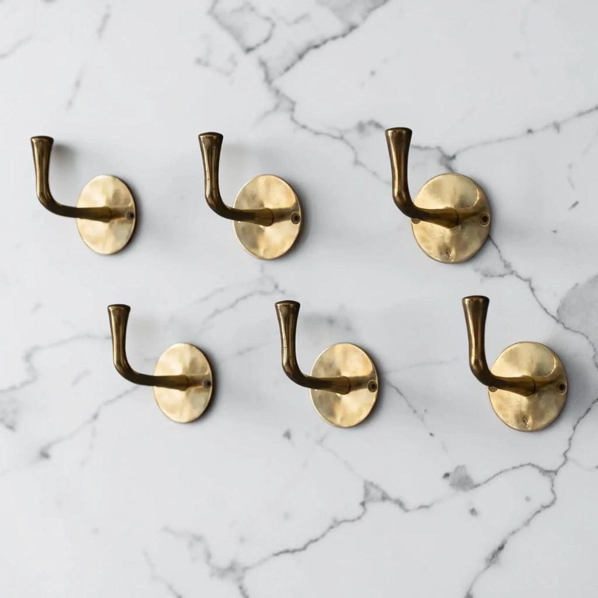 Set of six brass wall hooks on a marble background