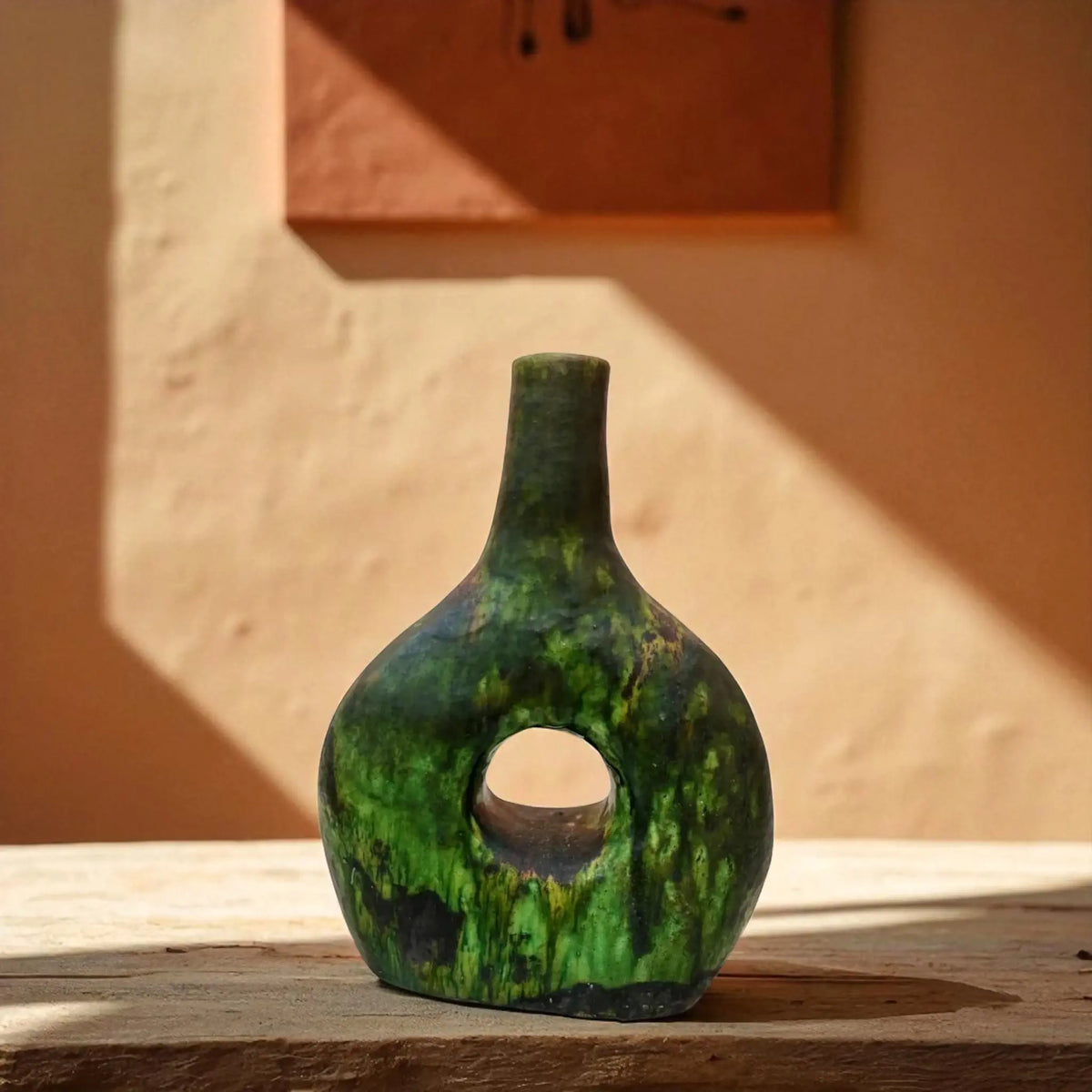 Green ceramic vase with a hole on a wooden surface with a warm-toned background