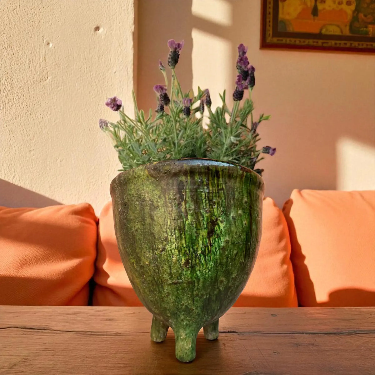 Green textured vase with lavender plant on a wooden surface with orange cushions in the background
