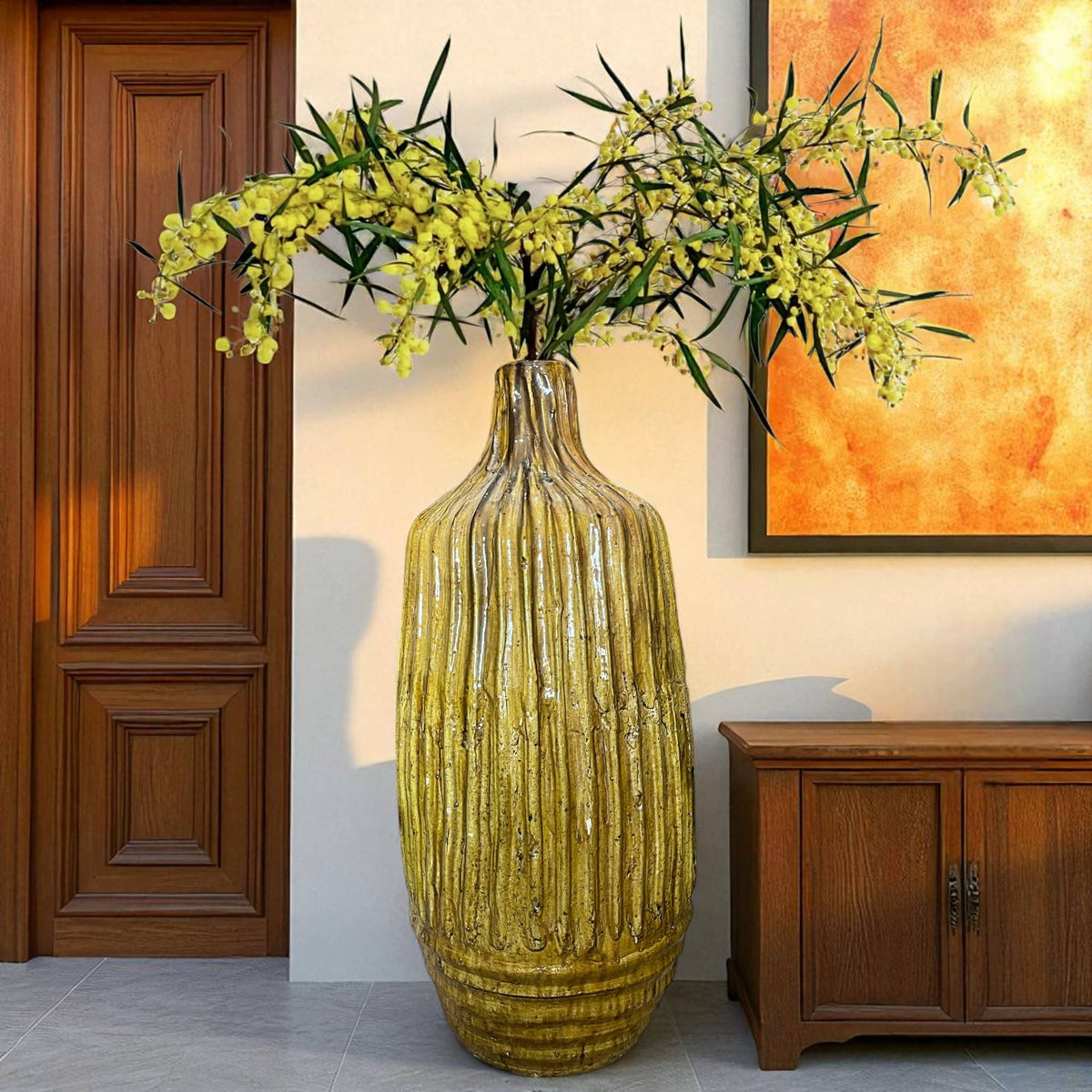 Yellow textured vase with flowers in a room with wooden door and cabinet.