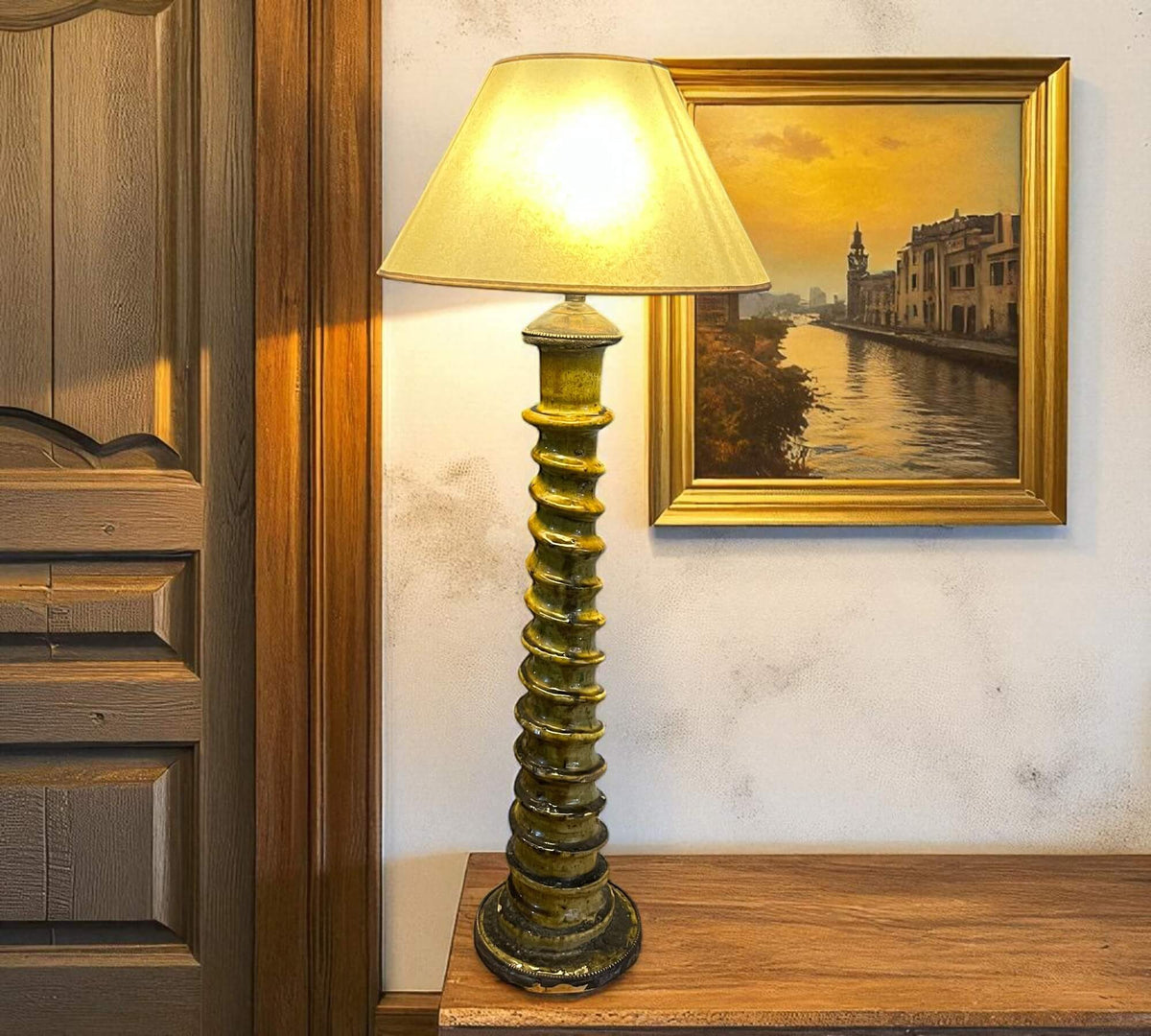 Decorative lamp on a wooden shelf with a painting of a canal scene in the background.