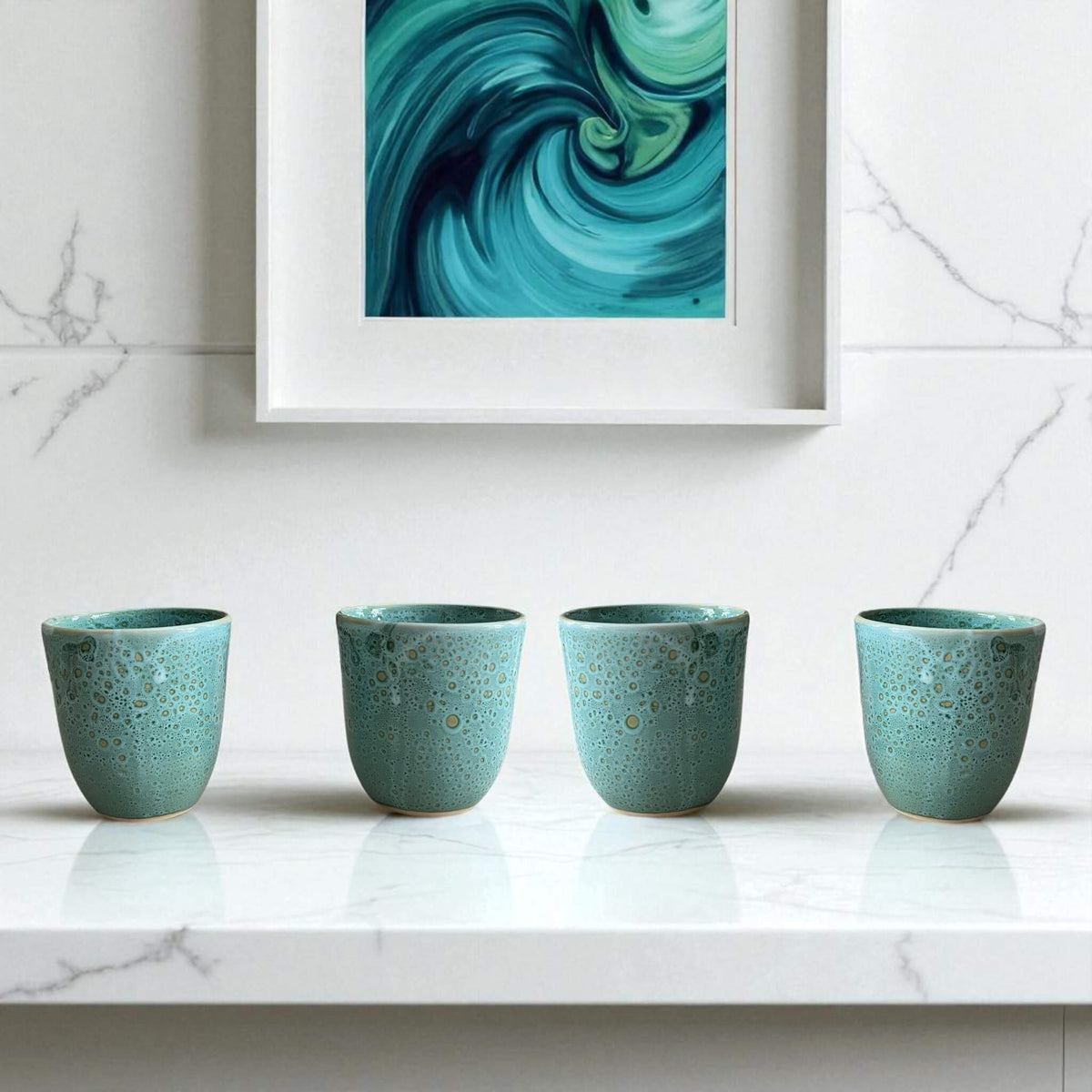 Four teal ceramic cups on a marble surface with a abstract teal painting in the background.