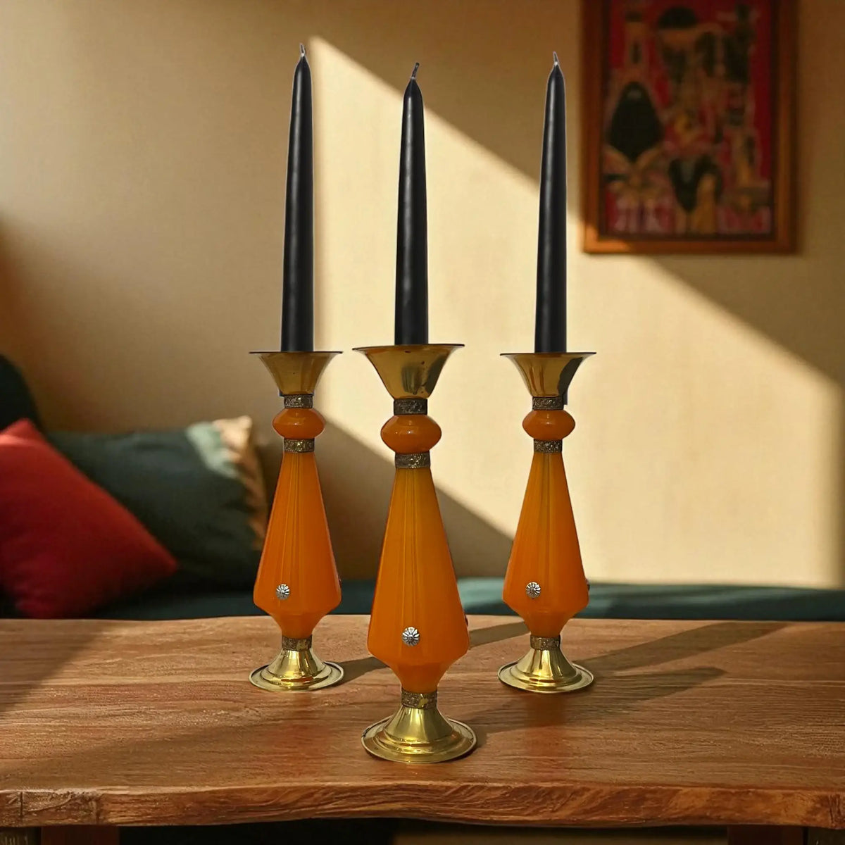 Three Amber resin and brass candlestick with flared top and sunburst medallion, 22 cm tall vintage decorative candle holder with black candles on a wooden surface.