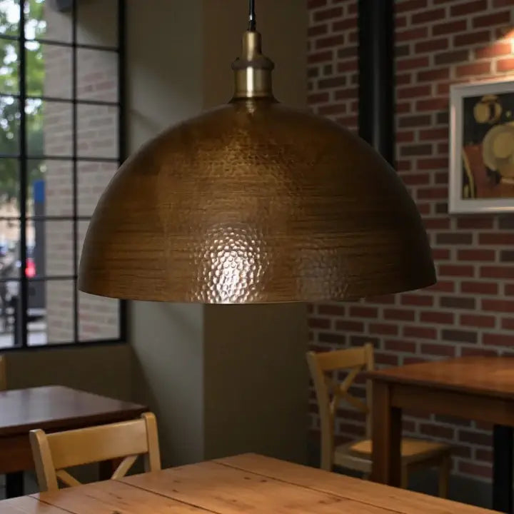Gold pendant lamp hanging above a wooden table in a restaurant setting with brick wall and window.