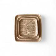Bronze-colored square dish with embossed design on a white background