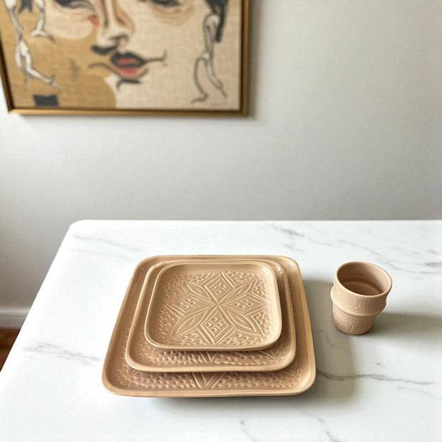 Set of ceramic trays and a cup on a marble surface with a wall art piece in the background.