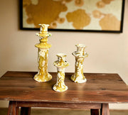 Three decorative candle holders on a wooden table with a blurred abstract painting in the background.