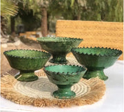 Set of four green ceramic bowls on a woven mat with a blurred natural background