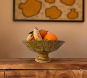 Fruit bowl with bananas and oranges on a wooden surface with a decorative wall in the background