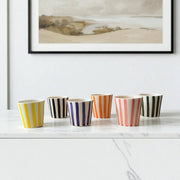 Set of colorful striped cups on a white surface with a framed landscape painting in the background.