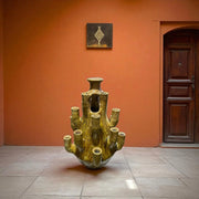 Cylindrical ceramic sculpture with multiple outlets against an orange wall.