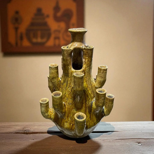 Cylindrical ceramic vase with multiple small openings on a wooden surface.