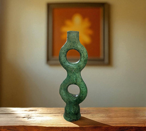 Green stone sculpture on a wooden surface with a blurred painting in the background