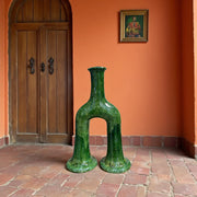 Green ceramic vase in a room with an orange wall and wooden door.