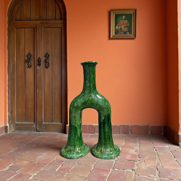 Green ceramic vase in a room with an orange wall and wooden door.