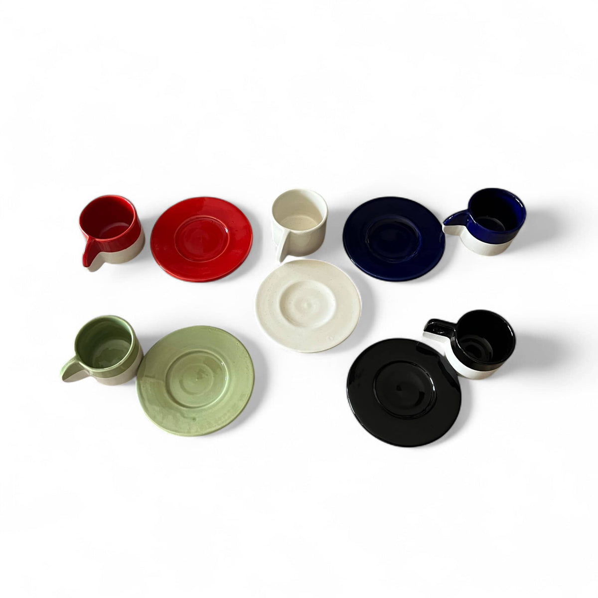 Set of ceramic cups and saucers in various colors on a white background