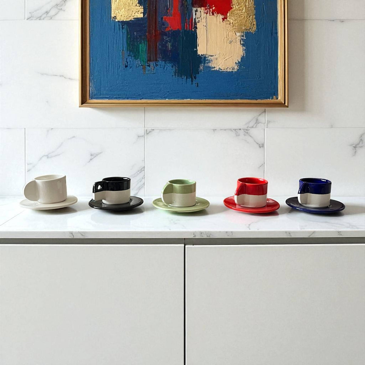 Set of colorful coffee cups and saucers on a marble countertop with abstract art in the background.