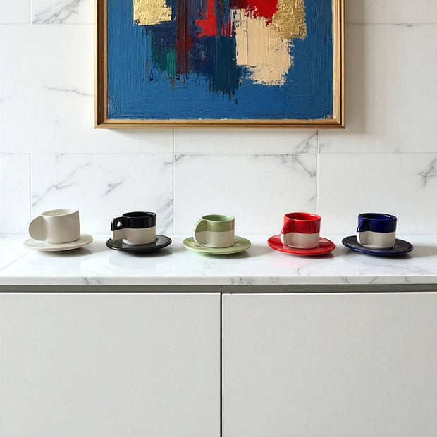 Set of colorful coffee cups and saucers on a marble countertop with abstract art in the background.