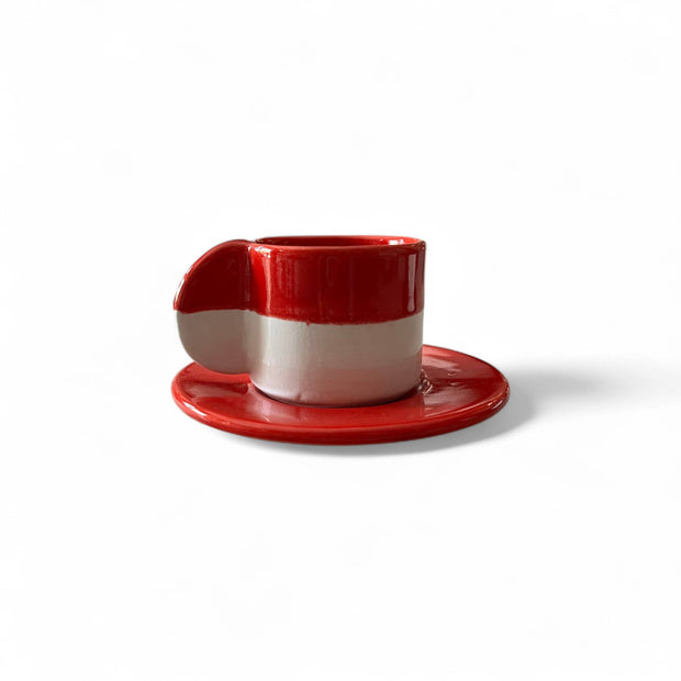 Red and white ceramic cup with saucer on a white background