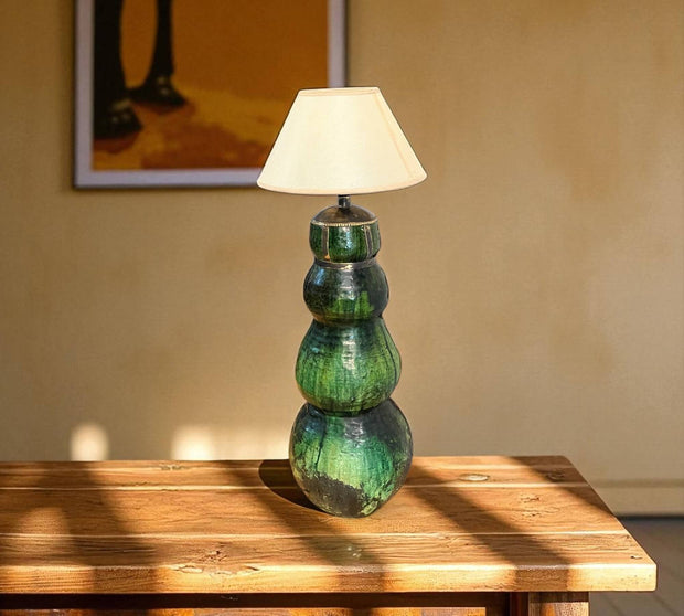 Green ceramic table lamp with a white shade on a wooden surface.