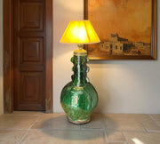 Green ceramic floor lamp with yellow lampshade in a room with a wooden door and framed artwork.
