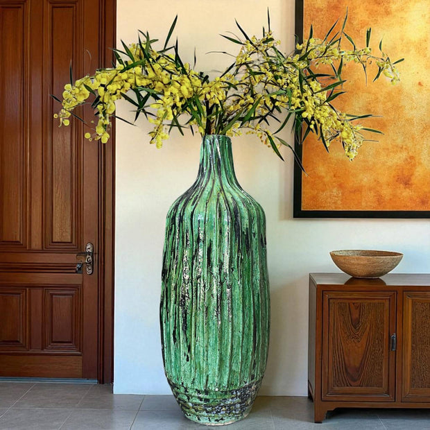 Green textured vase with yellow flowers in a room with wooden furniture and a painting.