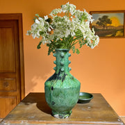 Green textured vase with white flowers on a wooden table against an orange wall.