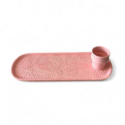 Pink ceramic tray with embossed design and matching cup on a white background