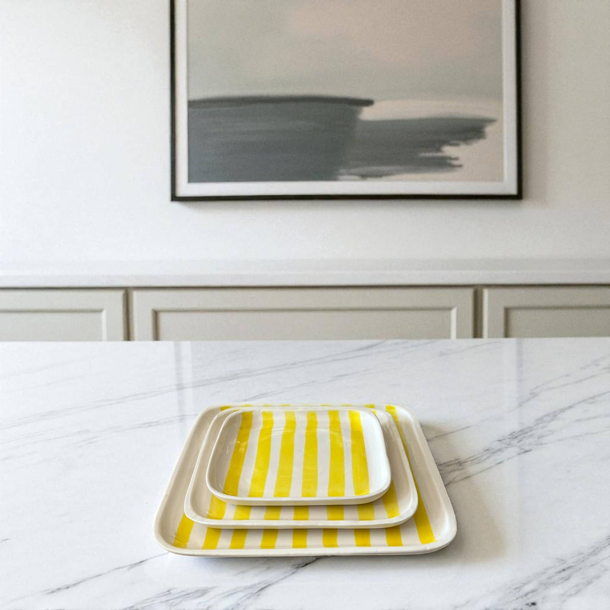 Yellow striped trays on a marble surface with a framed abstract painting in the background.