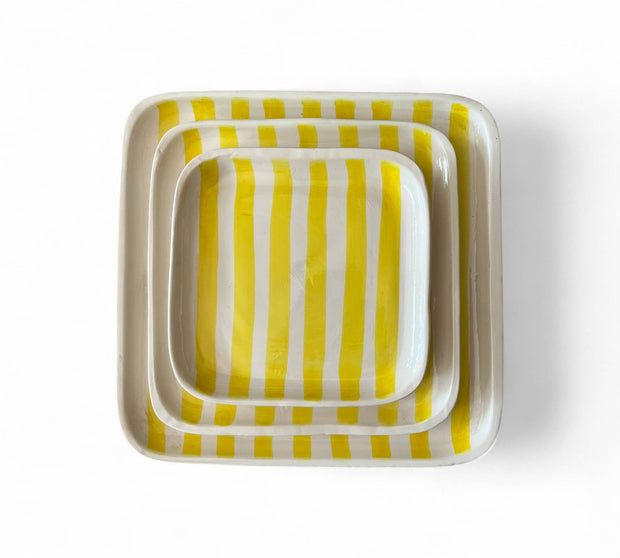 Set of three square ceramic trays with yellow and white striped pattern on a white background