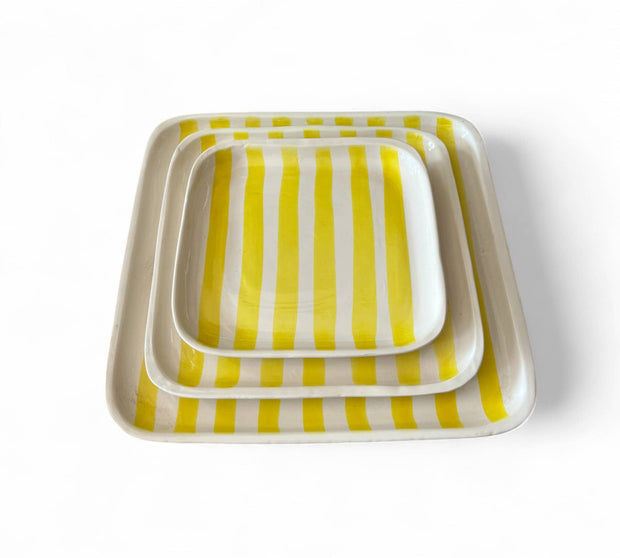 Set of three square trays with yellow and white striped pattern on a white background