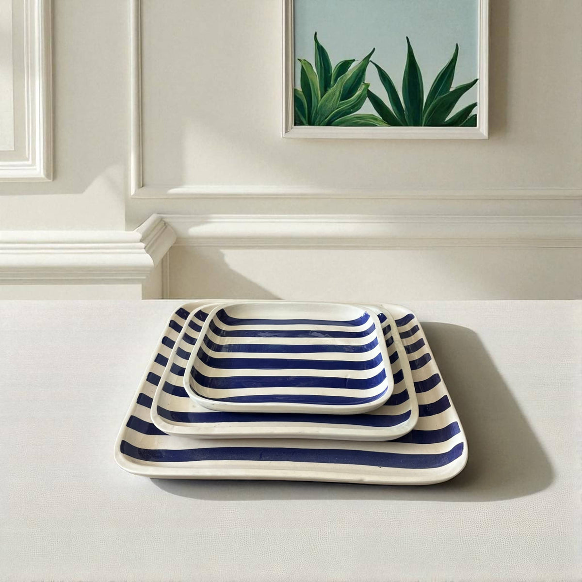 Set of three striped trays on a white surface with a framed plant picture in the background.