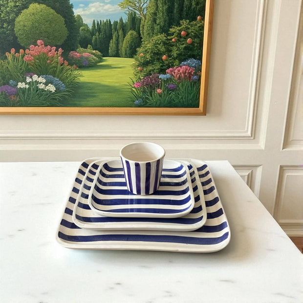 Blue and white striped ceramic set on a table with a garden painting in the background