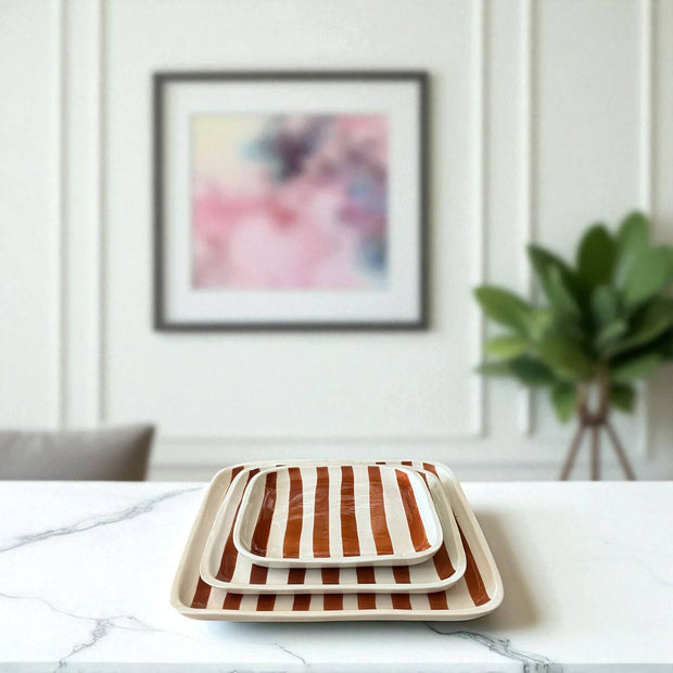Set of striped trays on a marble surface with a blurred abstract painting in the background.