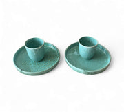 Two turquoise ceramic cups with matching saucers on a white background