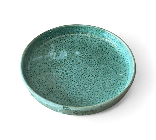 Turquoise ceramic bowl with a textured surface on a white background