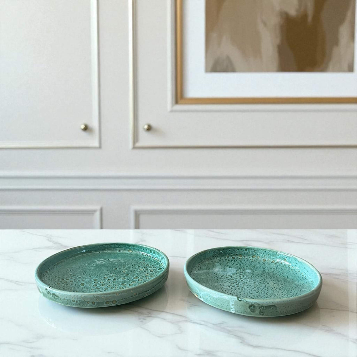 Two turquoise ceramic plates on a marble surface with a neutral-colored wall in the background.