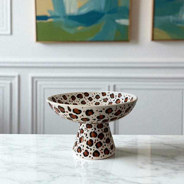 Ceramic bowl with leopard print design on a marble surface with a white wall and abstract art in the background.