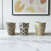 Three stacked ceramic pots with heart patterns on a marble surface, framed abstract art in the background.
