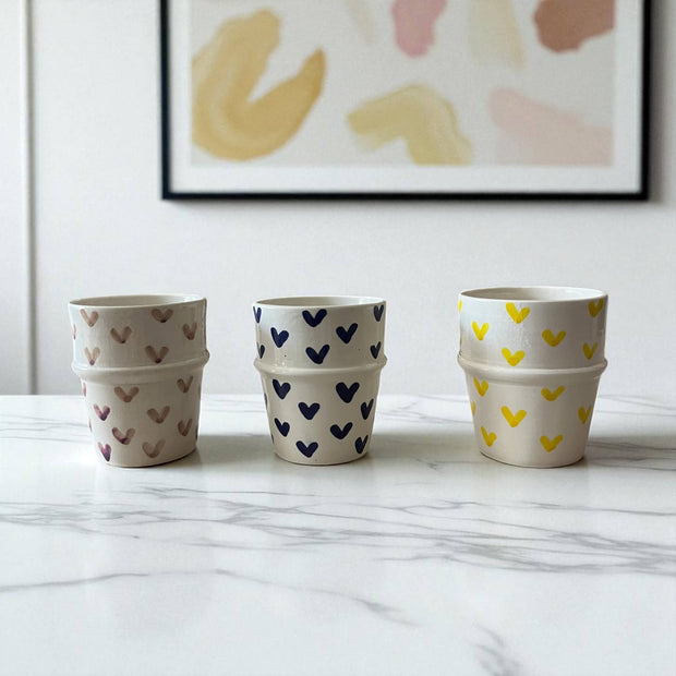 Three stacked ceramic pots with heart patterns on a marble surface, framed abstract art in the background.