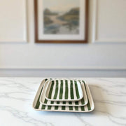 Set of three green and white striped ceramic trays on a marble surface with a framed picture in the background.