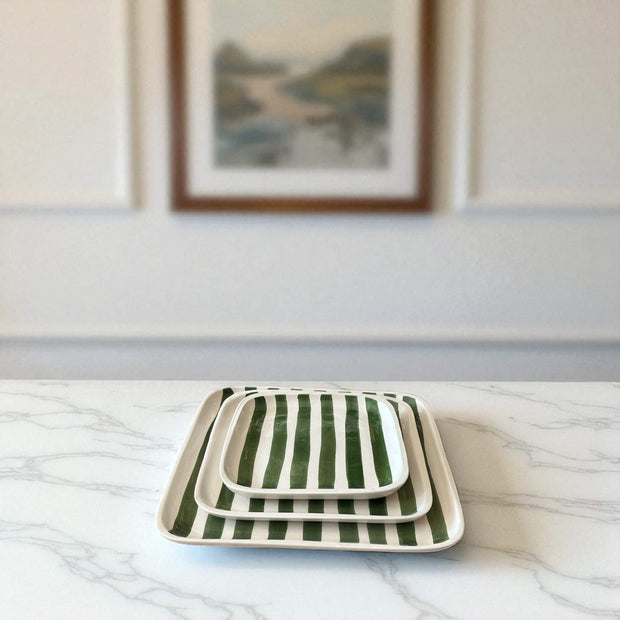 Set of three green and white striped ceramic trays on a marble surface with a framed picture in the background.